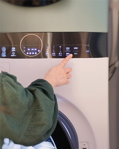 LG 트롬 오브제컬렉션 워시타워 컴팩트의 조작 패널을 터치하는 손의 클로즈업 이미지. 디스플레이에는 다양한 세탁 옵션이 표시되어 있으며, 제품의 세부적인 조작 기능이 강조된 모습.