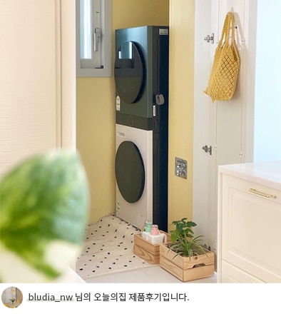 LG 트롬 오브제컬렉션 워시타워 컴팩트가 세탁실 안에 설치되어 있는 모습입니다. 공간 활용성을 강조한 제품으로 주변에는 화분과 세탁 액세서리가 배치되어 있습니다. 하단에는 'bludia_nw 님의 오늘의집 제품후기입니다.'라는 텍스트가 포함되어 있음.