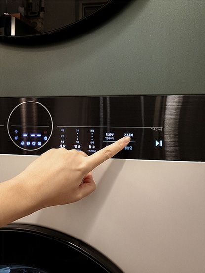 LG 트롬 오브제컬렉션 워시타워 컴팩트의 제어 패널을 손으로 터치하며 세탁 모드를 설정하는 모습입니다. LED 디스플레이에 표시된 다양한 세탁 옵션이 선명하게 보입니다.