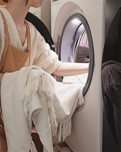 LG 트롬 오브제컬렉션 세탁기에서 빨래를 꺼내는 모습. 사용자가 세탁된 옷을 정리하고 있으며, 제품의 대용량 도어 디자인이 실용성을 강조함.