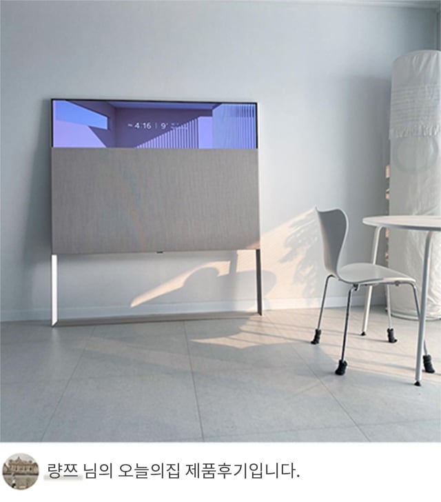 LG 올레드 오브제컬렉션 Easel TV가 하얀 벽을 배경으로 설치된 모습. 화면 상단에는 시간 '4:16 PM'이 표시되어 있음. 오른쪽 하단에는 의자와 작은 테이블이 보이며, 하단 텍스트는 '량쯔 님의 오늘의집 제품후기입니다.'라고 쓰여 있음