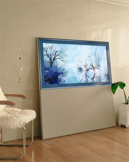 LG 올레드 오브제컬렉션 Easel TV가 무빙 커버를 아래로 내린 상태로, 화면에 자연 풍경 이미지가 출력된 모습. TV 앞에는 작은 나무 의자와 포근한 느낌의 인테리어 소품이 배치되어 아늑하고 세련된 공간을 강조함.