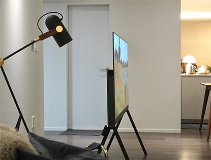 측면에서 본 LG 올레드 오브제컬렉션 Posé TV가 세련된 디자인을 보여주고 있는 모습. 주변에는 조명과 소파가 배치되어 따뜻한 거실 분위기를 연출함