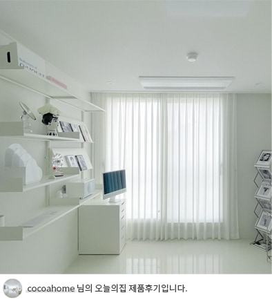 LG 휘센 주거용 시스템 에어컨이 설치된 밝은 화이트톤의 거실 혹은 방의 모습. 화면에는 모던한 가구와 선반이 조화를 이루고 있으며, 커튼이 설치된 창문을 통해 환한 채광이 들어옴. 하단에는 'cocoahome 님의 오늘의집 제품후기입니다.'라는 텍스트가 포함되어 있음. 