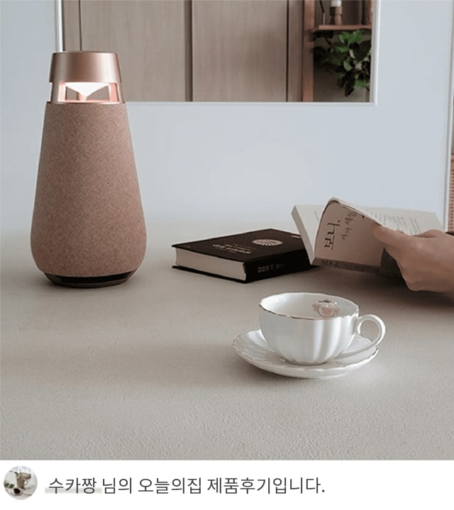 테이블 위에 놓인 커피잔과 받침, 책 두 권, 그리고 무드등 옆에서 책을 읽는 손의 모습. 배경에는 선반과 식물이 보이며, 하단에 '수카짱 님의 오늘의집 제품후기입니다.'라는 텍스트가 포함되어 있음.