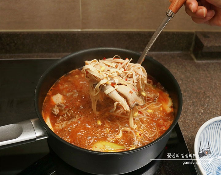 LG 디오스 인덕션 위에서 끓고 있는 마라탕 냄비에서 숙주와 버섯, 고기 등을 국자로 떠서 그릇에 담으려는 모습