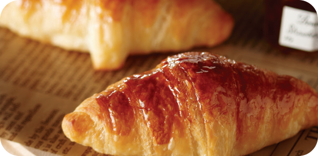 노릇하게 구어진 크루아상이 잼과 함께 신문 포장지 위에 올라가 있는 이미지