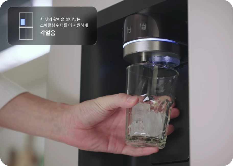 냉장고 디스펜서에서 투명한 유리컵에 일반 각얼음을 받고 있는 모습입니다. 이미지 상단에는 