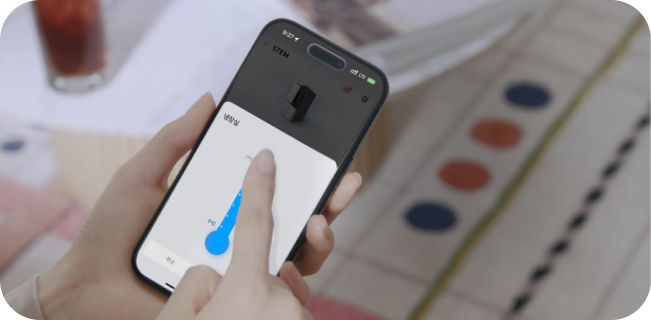 사용자가 스마트폰 앱(STEM)을 통해 냉장고의 설정을 제어하고 있는 모습입니다. 스마트폰 화면에는 '냉장실' 온도 조절 슬라이더를 손가락으로 조작하는 장면이 나타나 있습니다.