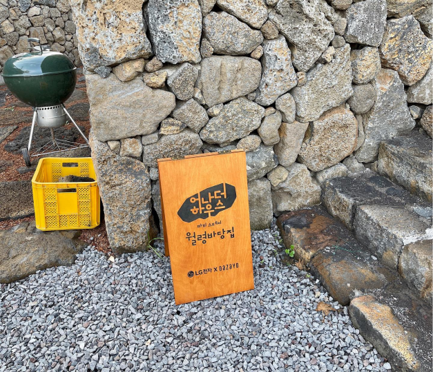 돌담 앞에 놓인 어나더 하우스 월령바당집 표지판