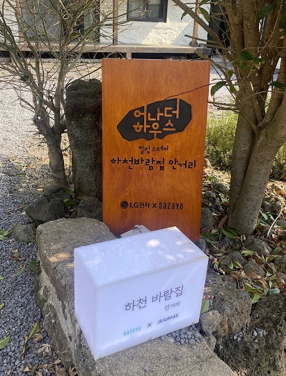 나무판에 새겨진 어나더 하우스 문구와 함께 작은 조명이 놓인 안내 표지판