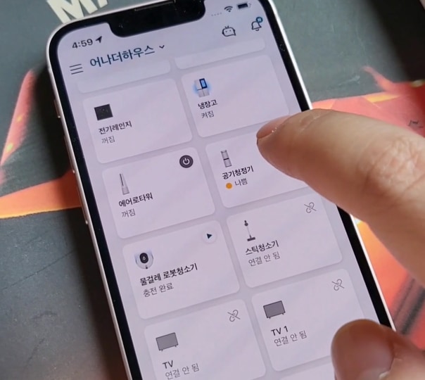 스마트폰 화면에 가전제품 제어 앱 실행 중, 손가락으로 공기청정기 상태 확인 