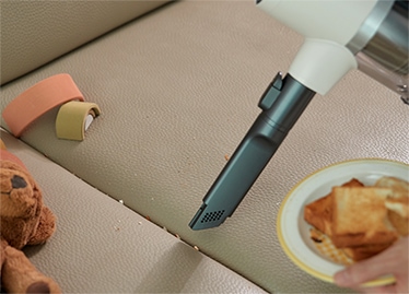 LG 코드제로 A9S 오브제컬렉션의 흡입구로 소파 주변의 작은 부스러기를 청소하는 모습. 깨끗한 실내를 유지하는 일상의 한 장면.