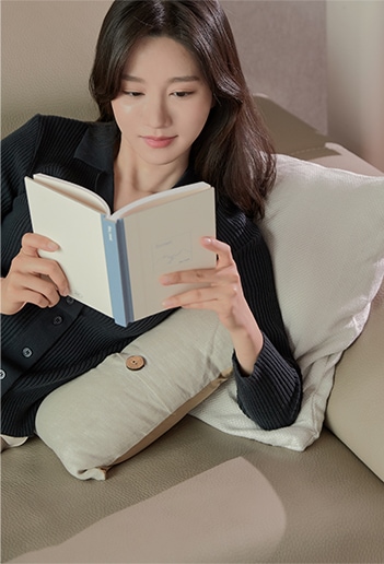 소파에 기대어 앉아 책을 읽는 여성. 편안한 자세로 독서에 집중하며 여유로운 시간을 보내는 모습.