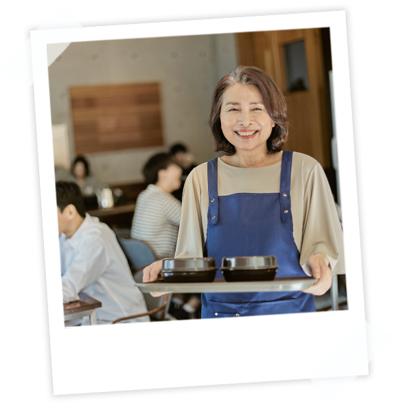 식당에서 일하는 여성이 환하게 웃으며 음식을 서빙하는 모습. 고객이 만족하는 환경을 상징.