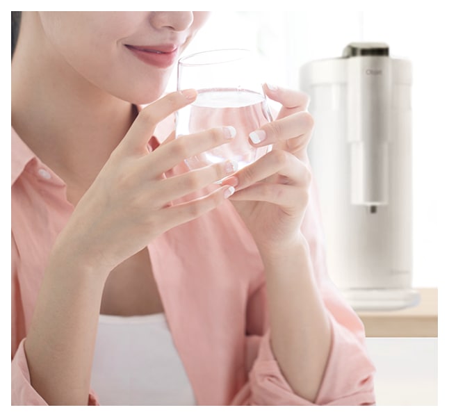 핑크색 셔츠를 입은 여성이 투명한 유리컵에 담긴 물을 두 손으로 들고 있는 모습