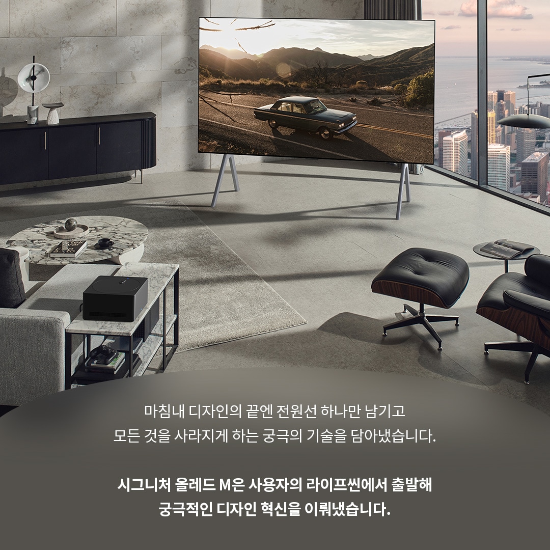 거실에 배치된 LG 시그니처 올레드 M TV와 그 앞에 위치한 원형 테이블, 편안한 의자들이 함께 어우러진 실내 공간. TV 화면에는 석양이 드리워진 도로와 자동차가 나타나며, 뒤로 도시와 자연 풍경이 보인다. 하단 텍스트는 제품의 미니멀리즘과 혁신적 디자인에 대해 설명한다.