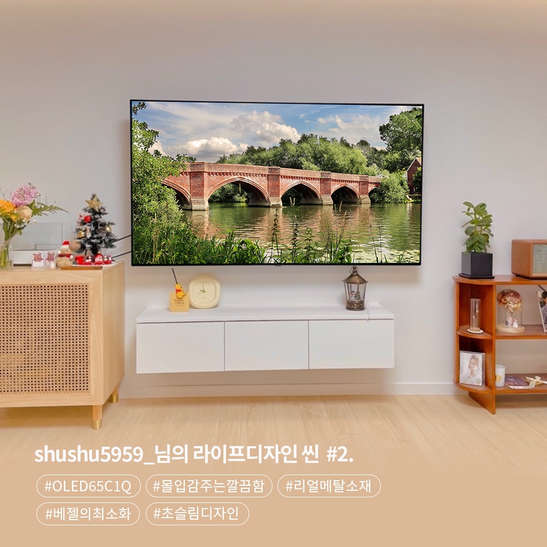 벽걸이형 LG OLED65C1Q TV가 설치된 거실로, 화면에는 강 위의 붉은 벽돌 다리와 자연 풍경이 나타난다. TV 아래에는 간결한 흰색 수납장이 있고, 왼쪽에 크리스마스 장식과 꽃병이 놓여 있으며, 오른쪽에는 책장이 자리하고 있다. 하단 텍스트는 제품 모델명과 디자인 요소를 언급한다.