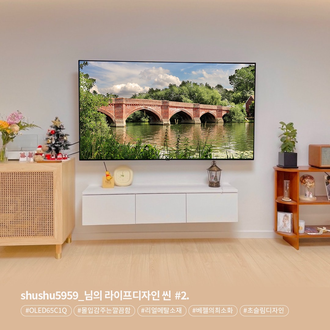 벽걸이형 LG OLED65C1Q TV가 설치된 거실로, 화면에는 강 위의 붉은 벽돌 다리와 자연 풍경이 나타난다. TV 아래에는 간결한 흰색 수납장이 있고, 왼쪽에 크리스마스 장식과 꽃병이 놓여 있으며, 오른쪽에는 책장이 자리하고 있다. 하단 텍스트는 제품 모델명과 디자인 요소를 언급한다.