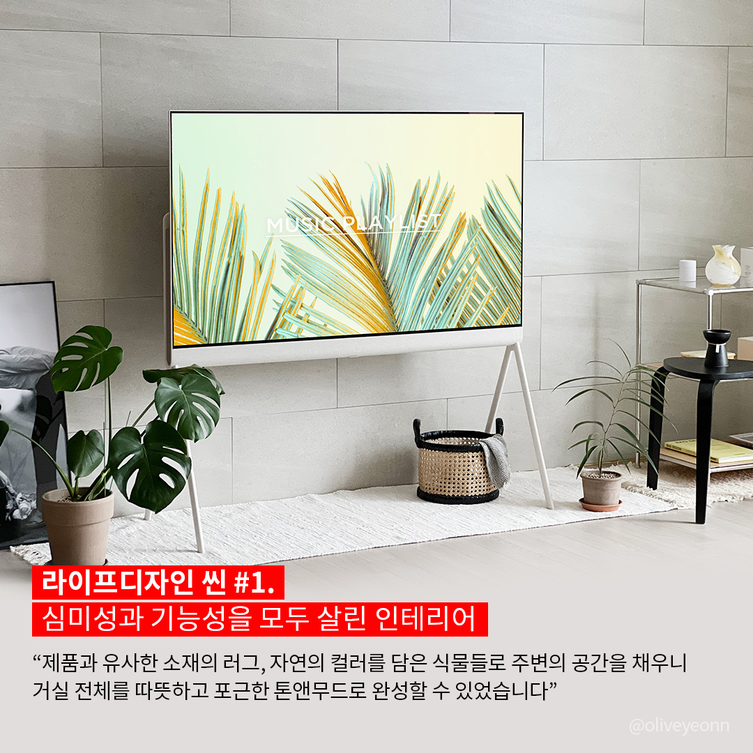 LG 라이프디자인 홍보 이미지. 미니멀한 디자인의 스탠드형 LG TV가 거실에 배치되어 있으며, 화면에는 'MUSIC · PLAY · HEAT'라는 텍스트와 함께 노란빛과 초록빛이 어우러진 야자수 잎 그래픽이 표시됨. 벽은 따뜻한 그레이 톤의 타일로 마감되어 있으며, TV 주변에는 다양한 크기의 화분과 식물들이 배치되어 자연 친화적인 분위기를 연출함. 좌측 바닥에는 액자가 기대어 있고, 우측에는 블랙 테이블과 투명 유리 선반이 배치됨. 화면 하단에는 '라이프디자인 씬 #1. 심미성과 기능성을 모두 살린 인테리어'라는 제목과 함께, 제품과 조화를 이루는 공간 구성에 대한 설명이 적혀 있음.