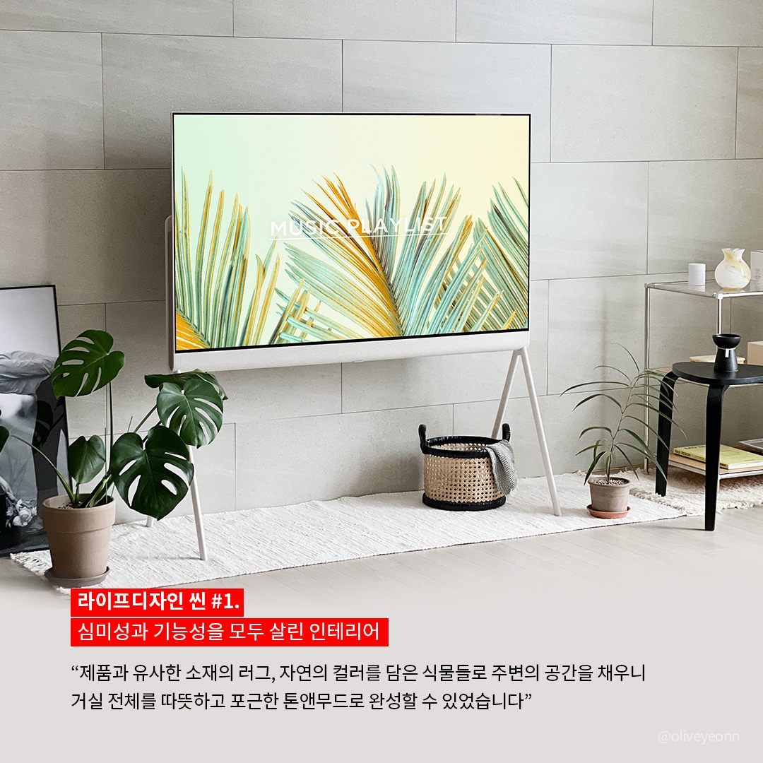 LG 라이프디자인 홍보 이미지. 미니멀한 디자인의 스탠드형 LG TV가 거실에 배치되어 있으며, 화면에는 'MUSIC · PLAY · HEAT'라는 텍스트와 함께 노란빛과 초록빛이 어우러진 야자수 잎 그래픽이 표시됨. 벽은 따뜻한 그레이 톤의 타일로 마감되어 있으며, TV 주변에는 다양한 크기의 화분과 식물들이 배치되어 자연 친화적인 분위기를 연출함. 좌측 바닥에는 액자가 기대어 있고, 우측에는 블랙 테이블과 투명 유리 선반이 배치됨. 화면 하단에는 '라이프디자인 씬 #1. 심미성과 기능성을 모두 살린 인테리어'라는 제목과 함께, 제품과 조화를 이루는 공간 구성에 대한 설명이 적혀 있음.