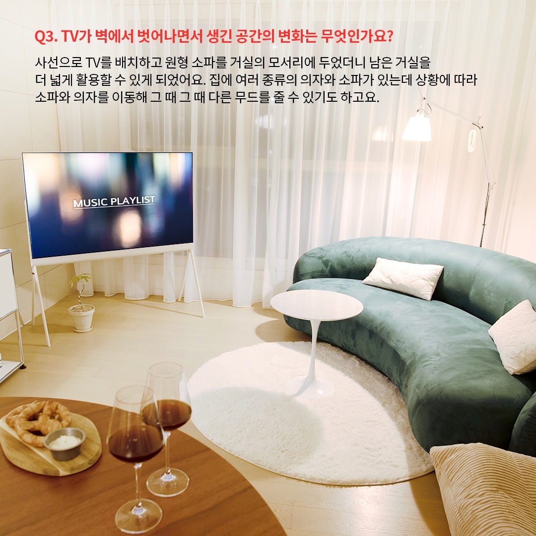 밝은 거실에 Music Playlist라는 텍스트가 표시된 올레드 TV가 배치되어 있으며, 둥근 소파와 화이트 테이블이 조화를 이루는 모습. TV를 벽이 아닌 독립형으로 배치하여 공간을 더 효율적으로 활용할 수 있음을 보여줍니다. 주된 내용은 가구 배치의 자유로움과 TV 배치 변화가 공간 분위기를 어떻게 개선하는지를 설명합니다.