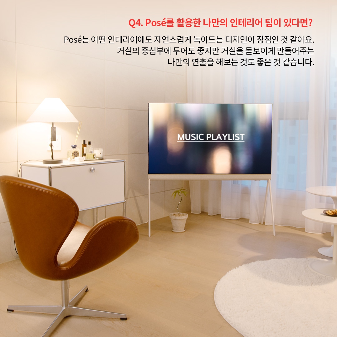 올레드 TV가 거실 중앙에 놓여 있고 Music Playlist 화면이 표시되어 있으며, 옆에는 갈색의 의자와 화이트 테이블이 조화를 이루고 있습니다. Posé TV를 활용하여 거실의 중심부를 연출하면서도 자연스럽게 공간과 어우러지도록 배치한 사례를 보여줍니다.