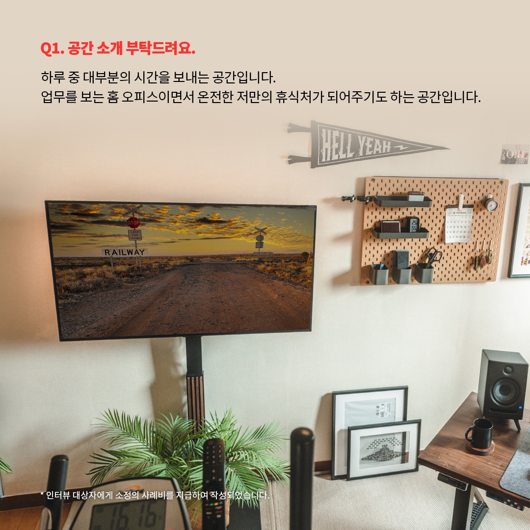 홈 오피스이자 개인 휴식 공간으로 구성된 인테리어 이미지로, 벽걸이형 LG OLED TV에는 기차 철길이 보이는 자연 풍경이 표시된 모습. ‘Q1. 공간 소개 부탁드려요. 하루 중 대부분의 시간을 보내는 공간입니다. 업무를 보는 홈 오피스이면서 온전한 저만의 휴식처가 되어주기도 하는 공간입니다. *인터뷰 대상자에게 소정의 사례비를 지급하여 작성되었습니다.’ 라는 문구가 포함되어 있음.