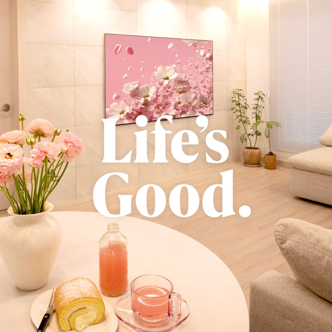 아늑한 거실에 벽 밀착형 LG OLED TV가 설치되어 핑크빛 꽃잎 화면을 띄우고. 테이블 위에는 꽃, 롤케이크, 핑크빛 음료가 놓여 감성적인 분위기를 연출하며, 'Life’s Good.' 문구가 강조됨.