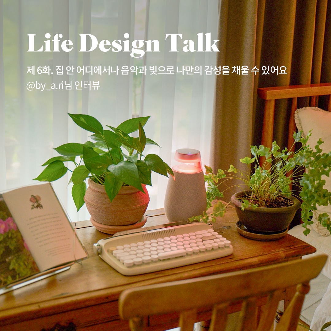 Life Design Talk 제 6화. 집 안 어디에서나 음악과 빛으로 나만의 감성을 채울 수 있어요 @by_a.ri님 인터뷰 문구 표시됨. 배경은 우드 테이블 위에 식물 화분과 키보드가 놓여 있으며, 창가에는 흰색 커튼이 드리워짐. 따뜻한 분위기의 조명과 초록빛 식물이 조화를 이룸.