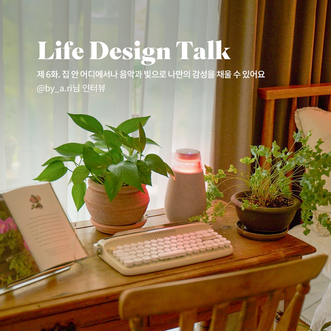 Life Design Talk 제 6화. 집 안 어디에서나 음악과 빛으로 나만의 감성을 채울 수 있어요 @by_a.ri님 인터뷰 문구 표시됨. 배경은 우드 테이블 위에 식물 화분과 키보드가 놓여 있으며, 창가에는 흰색 커튼이 드리워짐. 따뜻한 분위기의 조명과 초록빛 식물이 조화를 이룸.