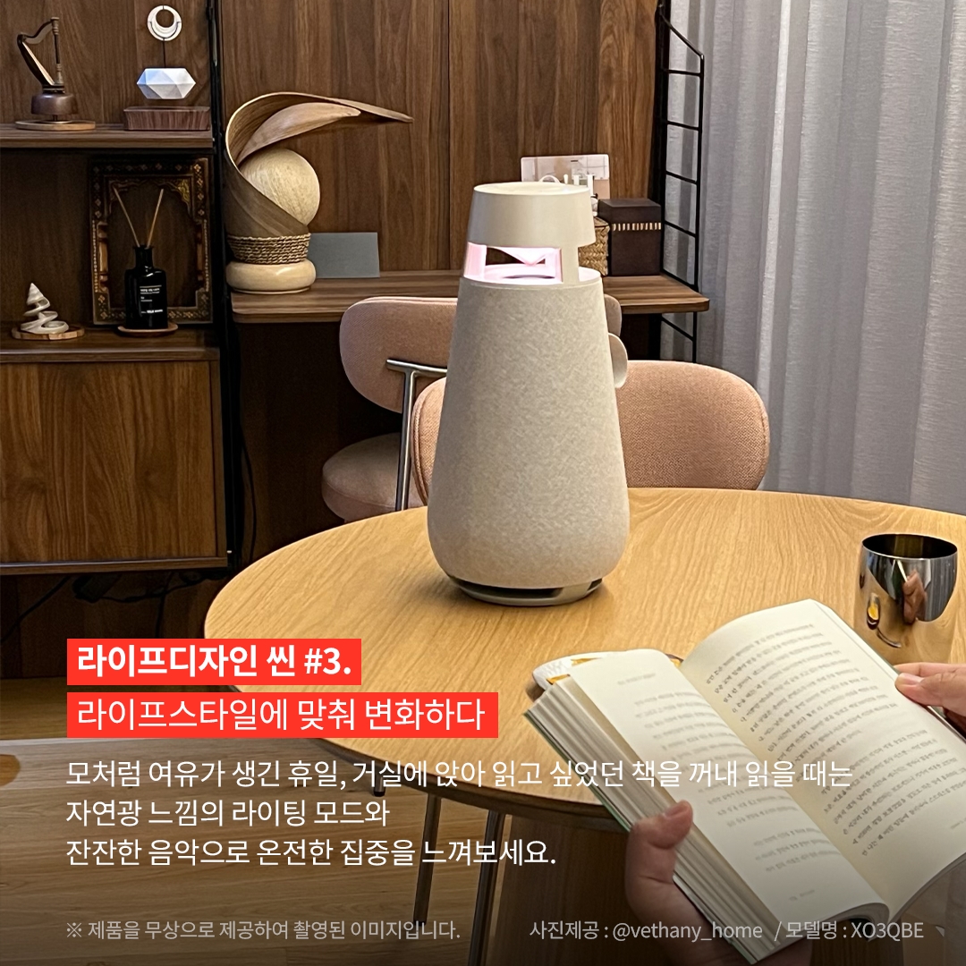 라이프디자인 씬 3. 라이프스타일에 맞춰 변화하다 모처럼 여유가 생긴 휴일, 거실에 앉아 읽고 싶었던 책을 꺼내 읽을 때는 자연광 느낌의 라이팅 모드와 잔잔한 음악으로 온전한 집중을 느껴보세요. ※ 제품을 무상으로 제공하여 촬영된 이미지입니다. 사진제공: @vethany_home / 모델명: XO3QBE 문구 표시됨. 배경은 목재 테이블 위에 모래색 엑스붐 360 스피커가 놓여 있으며, 조명이 은은한 붉은빛을 내고 있음. 앞쪽에는 책을 읽는 손이 보이며, 배경에는 목재 책장과 장식품, 커튼이 있는 아늑한 실내 공간이 보임.