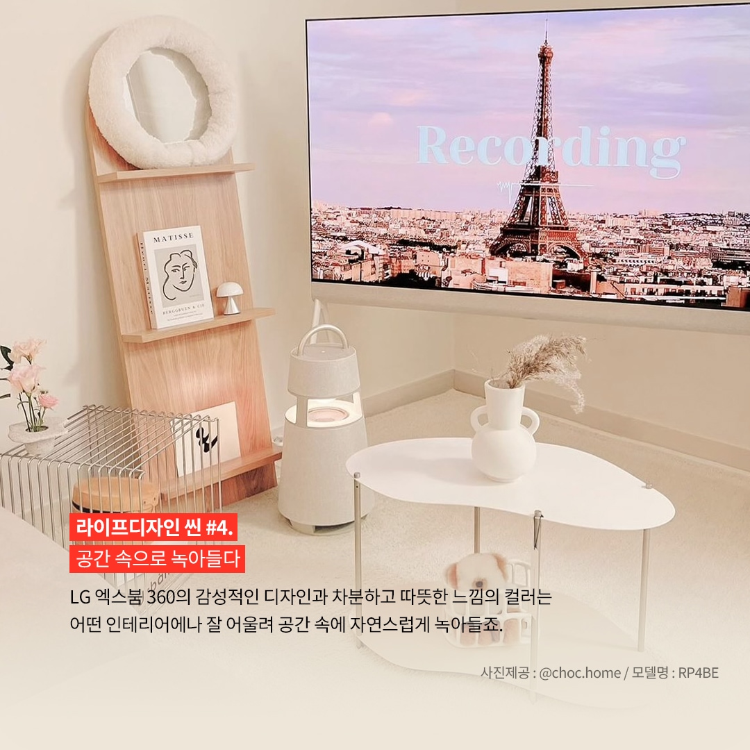 라이프디자인 씬 4. 공간 속으로 녹아들다 LG 엑스붐 360의 감성적인 디자인과 차분하고 따뜻한 느낌의 컬러는 어떤 인테리어나 잘 어울려 공간 속에 자연스럽게 녹아들죠. 사진제공: @choc.home / 모델명: RP4BE 문구 표시됨. 배경은 밝은 실내에서, 흰색 원형 테이블과 나무 선반, 그리고 선반 위의 장식들이 보임. 선반에는 그림과 소품이 있으며, 바닥에는 엑스붐 360 스피커가 놓여 있음. 대형 TV에서 에펠탑이 보이는 화면이 나오고 있음.