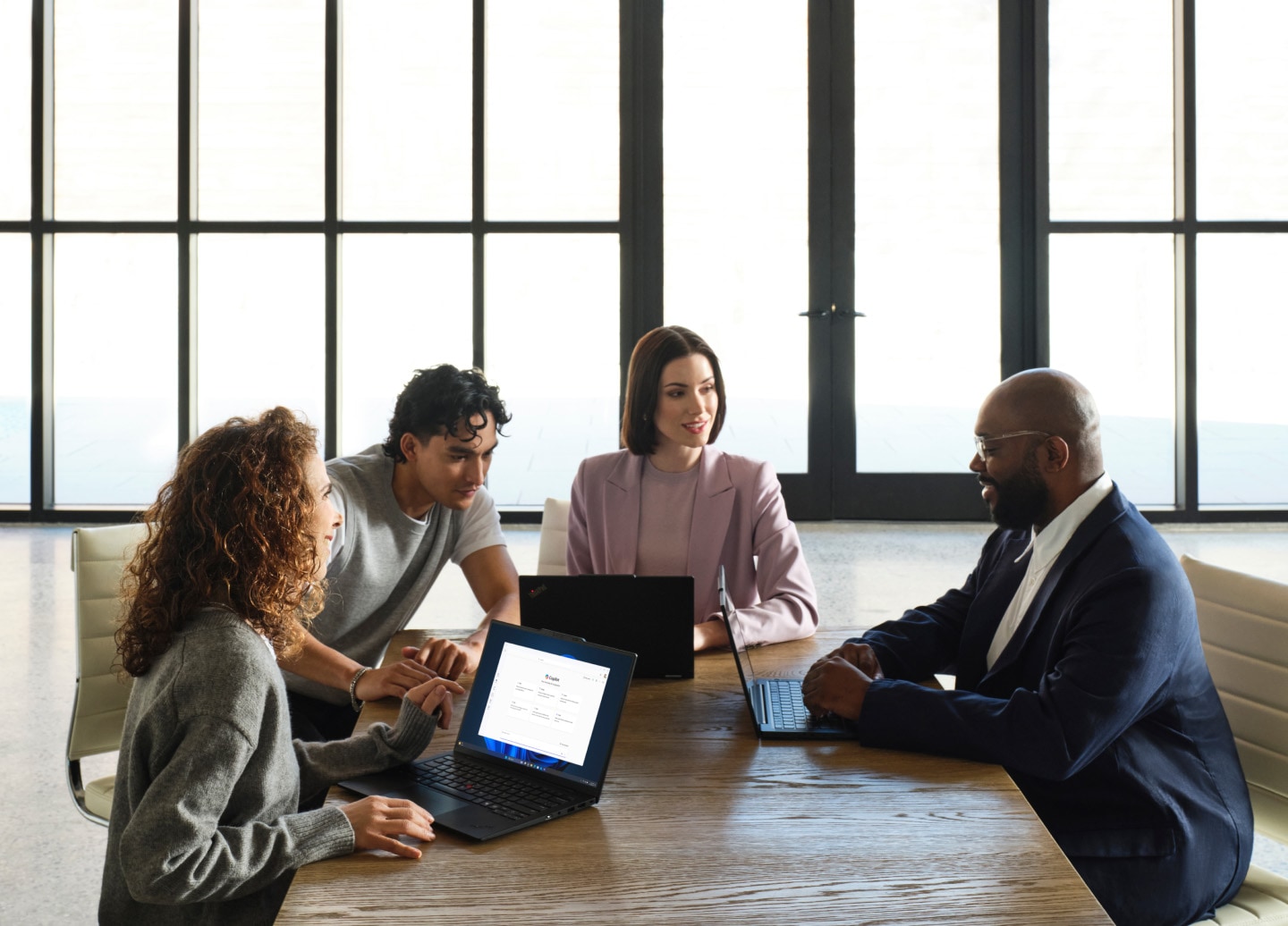 네 명의 사람들이 책상에 둘러앉아 노트북을 사용하며 회의하고 있는 모습.