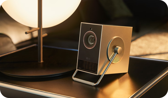 세련된 디자인의 LG 시네빔 프로젝터가 조명이 켜진 테이블 위에 놓여 있는 모습.