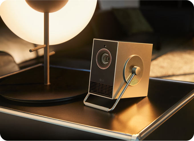 세련된 디자인의 LG 시네빔 프로젝터가 조명이 켜진 테이블 위에 놓여 있는 모습.