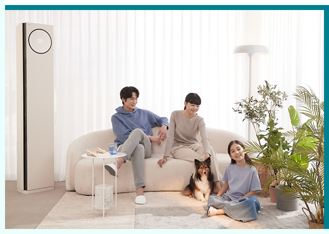 밝은 거실 공간에 가족이 함께 있는 모습. 커튼이 드리워진 창가 옆에 LG 에어로타워가 놓여 있으며, 베이지색 소파에 앉은 두 성인과 바닥에 앉아 있는 아이가 반려견과 함께 시간을 보내고 있다. 오른쪽에는 다양한 화분 식물이 놓여 있어 따뜻하고 아늑한 분위기를 연출한다.