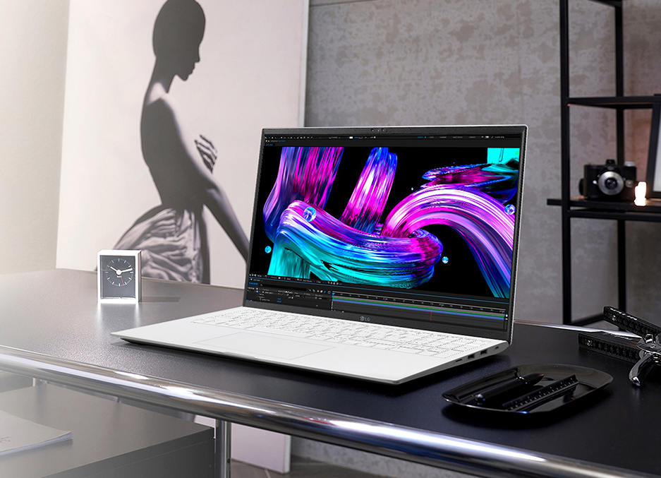 디자인 작업용으로 사용 중인 LG 그램 Pro 노트북이 책상 위에 놓여 있습니다. 화면에는 화려한 색상의 그래픽 작업물이 표시되어 있으며, 배경에는 흑백 실루엣 포스터와 카메라가 보이는 인테리어 소품이 배치되어 있습니다.