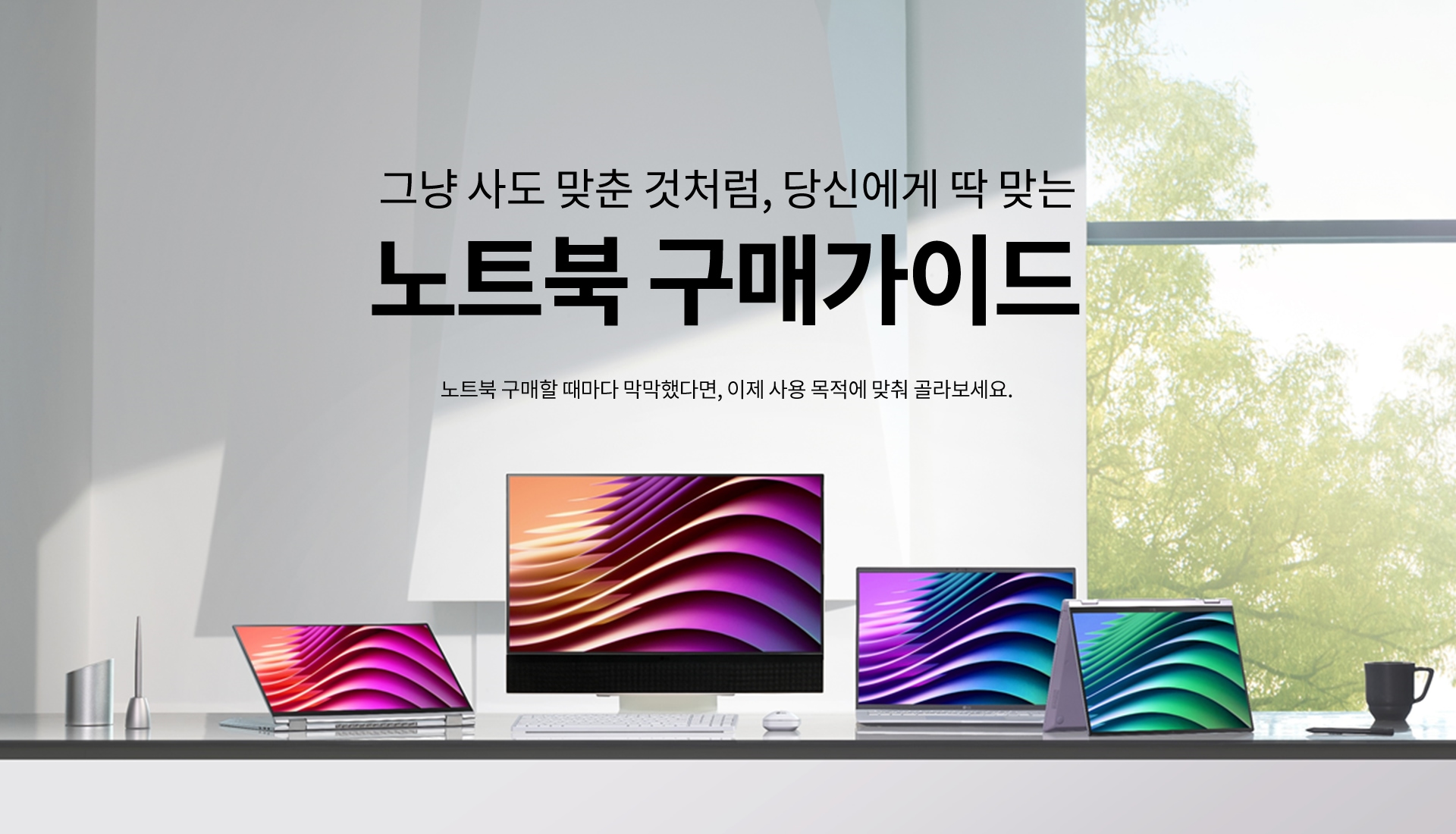 밝은 실내 창가 테이블 위에 다양한 디자인의 노트북과 모니터가 진열되어 있습니다. 상단에는 '그냥 사도 맞춘 것처럼, 당신에게 딱 맞는 노트북 구매가이드'라는 문구가 크게 적혀 있고, 그 아래에 '노트북 구매할 때마다 막막했다면, 이제 사용 목적에 맞춰 골라보세요.'라는 설명이 있습니다. 배경 창문 너머로는 푸른 나무들이 보이며 자연 채광이 들어오는 공간입니다.