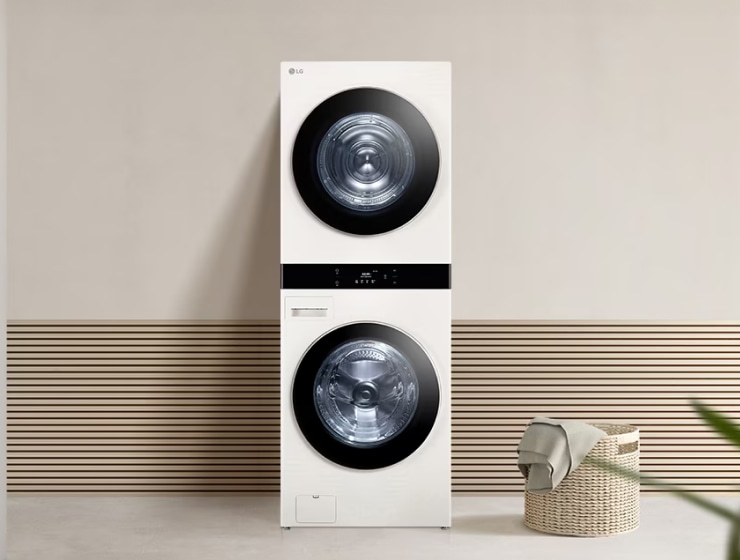 LG 워시타워. 흰색 건조기와 세탁기가 세로로 쌓여 있는 타워형 제품이며, 주변에 세탁 바구니와 수건이 놓여 있습니다.