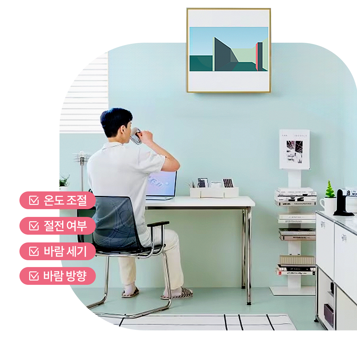 벽에 설치된 액자형 LG 아트쿨 에어컨 아래에서 남성이 책상에 앉아 음료를 마시는 모습, 왼쪽에는 온도 조절, 절전 여부, 바람 세기, 바람 방향이라고 적혀 있는 모습.