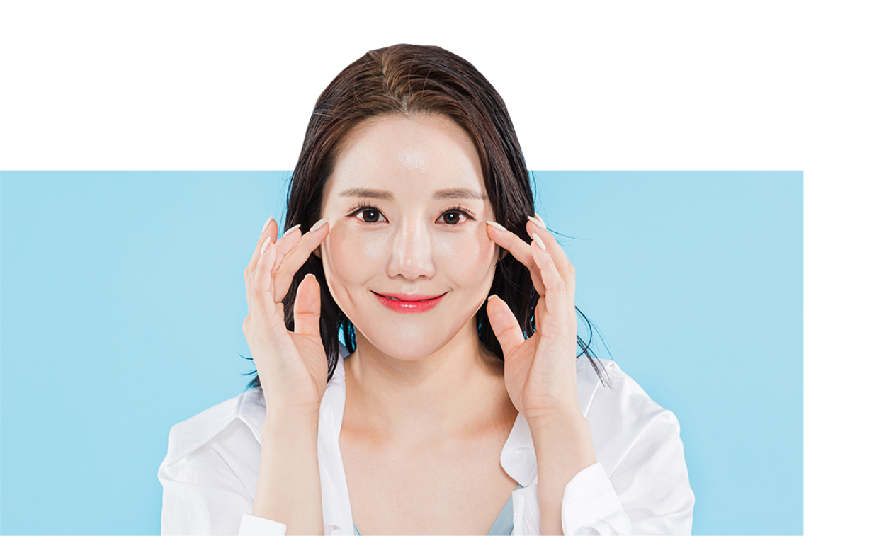 밝은 파란색 배경 앞에서 환하게 미소 짓는 여성이 양 손으로 눈 주위를 터치하고 있는 모습.