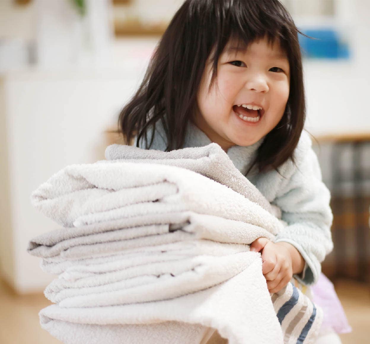 어린아이가 환하게 웃으며 여러 장의 깨끗한 흰색 수건을 안고 있음.