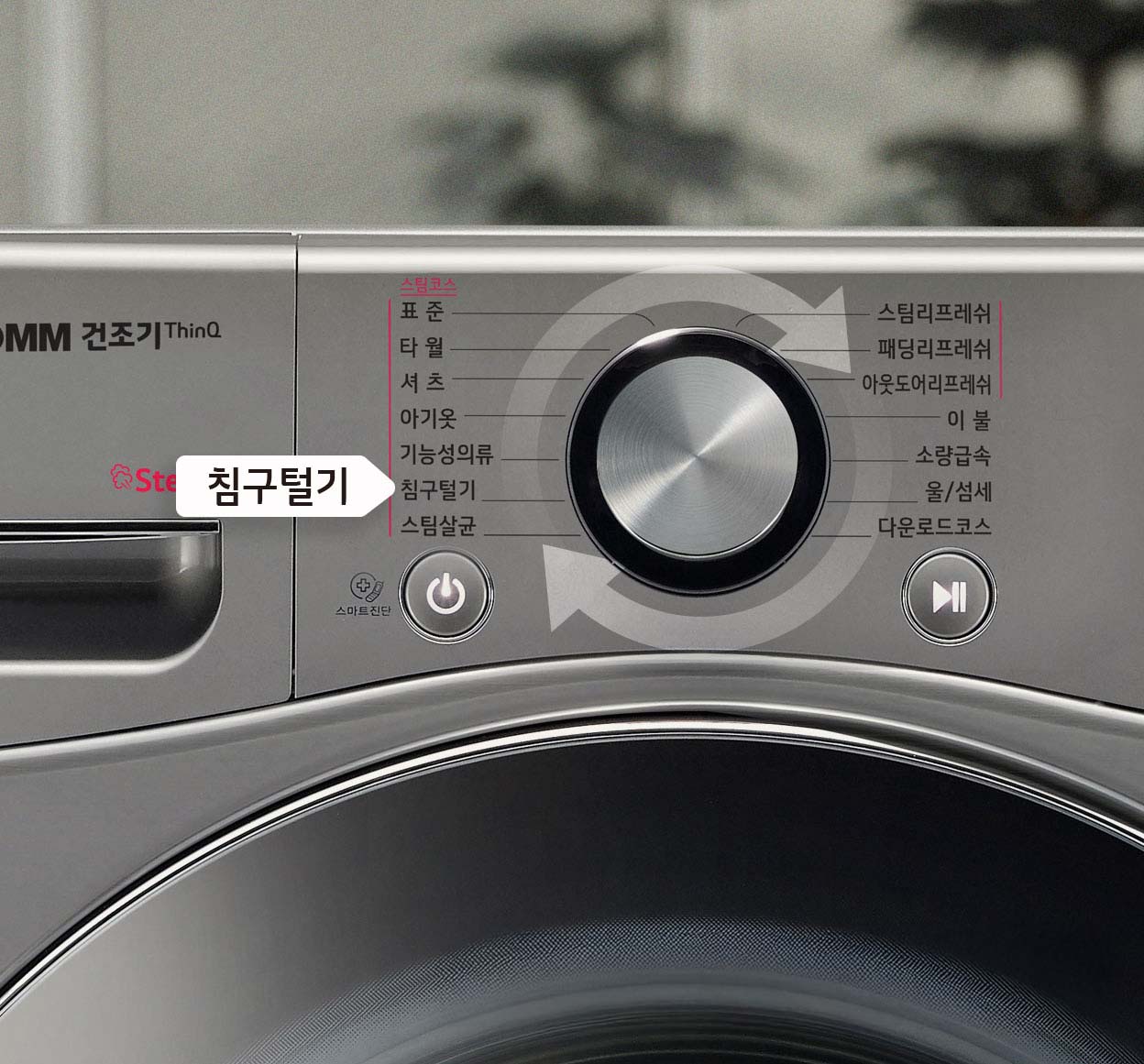 스테인리스 디자인의 LG 트롬 건조기 조작 패널 클로즈업, 중앙에 다이얼이 있고 다양한 건조 코스 옵션이 나열됨. 침구털기 코스가 강조.