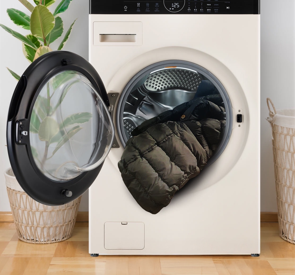 LG 드럼 세탁기의 문이 열려 있으며, 검은색 패딩이 내부에서 일부 나와 있음. 배경에는 초록색 식물과 라탄 바구니가 배치되어 있음.
