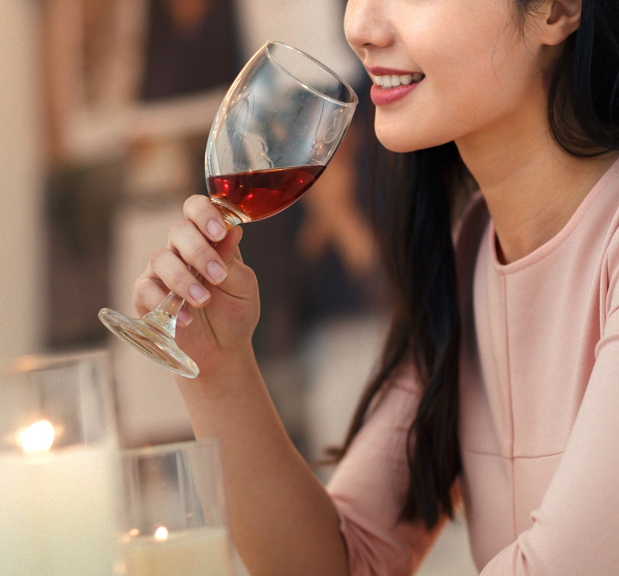 와인 잔을 들고 미소 짓는 여성의 모습이며, 테이블 위에는 촛불이 놓여 있음.