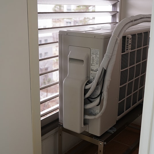 실내 창문 앞에 놓인 에어컨 실외기, 배관이 연결됨