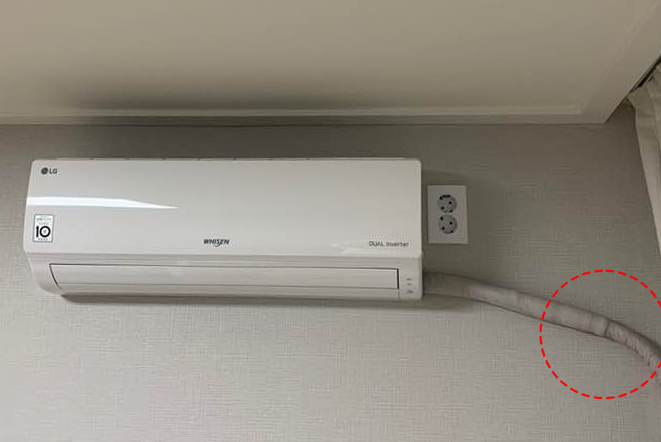 벽걸이형 에어컨이 설치되어 있고, 배관이 벽을 따라 정리됨