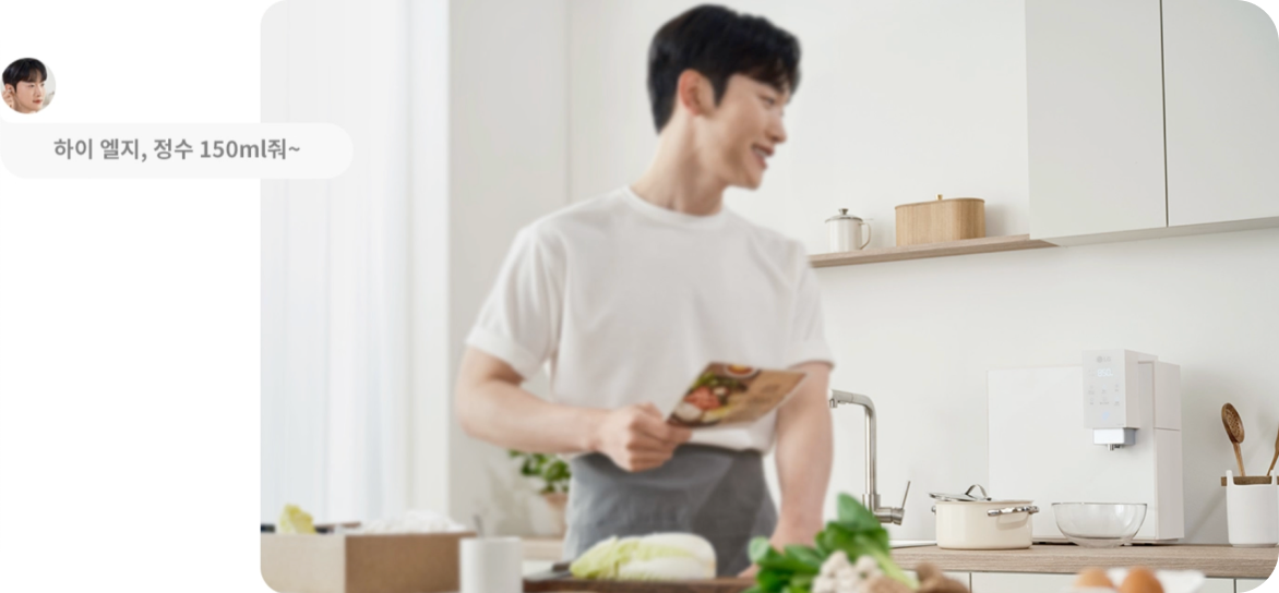 화이트톤의 주방에서 남성이 레시피 책을 들고 요리를 준비하며 미소 짓고 있습니다. 벽면에는 LG 정수기가 설치되어 있으며, 화면 왼쪽에는 '하이 엘지, 정수 150ml 줘~'라는 음성 명령 텍스트가 표시되어 있습니다.