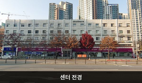 서초서비스센터의 서비스센터 건물은 가로로 길고 작은 유리창이 일정하게 배치되어 있습니다. 건물 중앙 꼭대기에는 '반포쇼핑타운2동'이라고 적혀있으며, 건물 1층 간판에 흰색 글씨, 분홍색 바탕으로 'LG전자 BEST SHOP 베스트샵', 'BEST 서비스센터'라고 쓰여 있습니다.